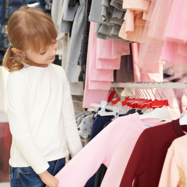 Fashion children clothing on hangers in rows at department store. Young, beautiful, pretty girl looking and choosing pink blouse in stylish boutique. Children vogue and style.